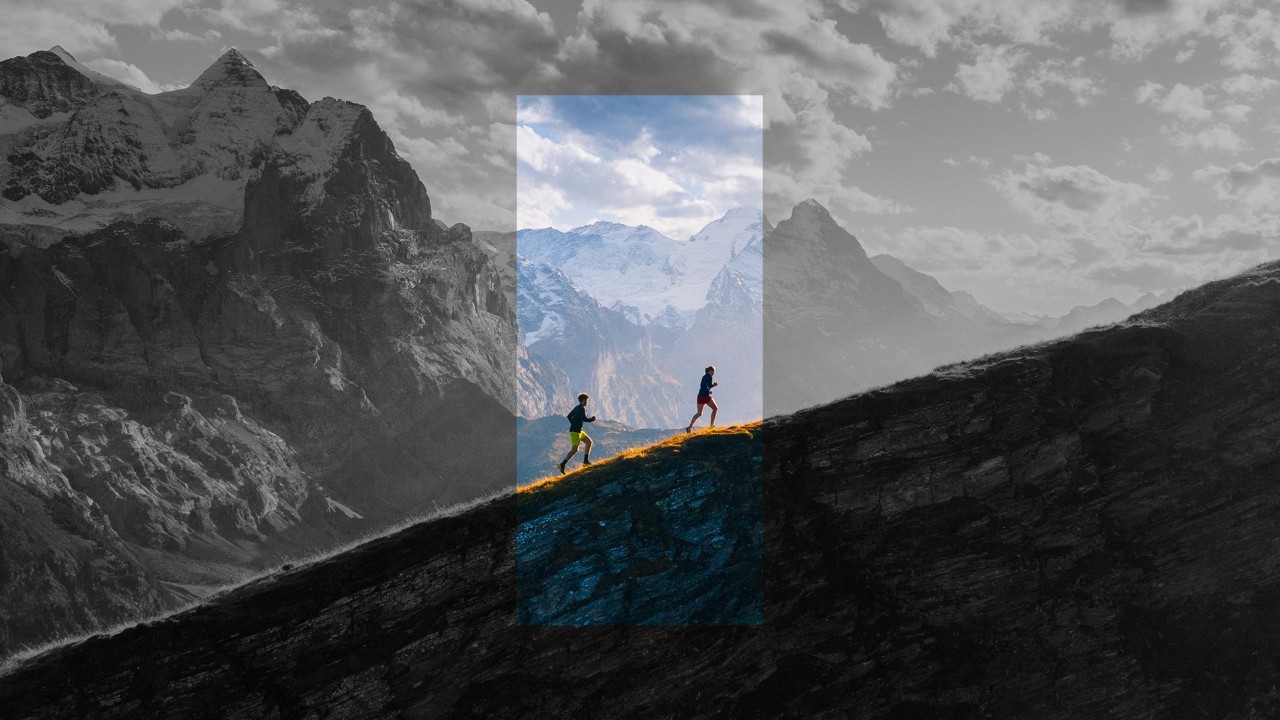 two people hiking up a mountain with bigger mountains in the background